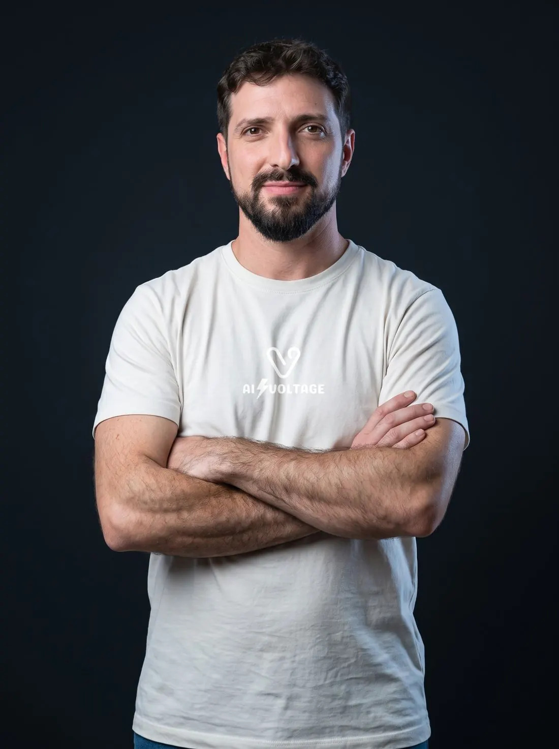Junior, fundador da AI Voltage, de braços cruzados com a camiseta da marca, sorrindo para a câmera sobre fundo escuro